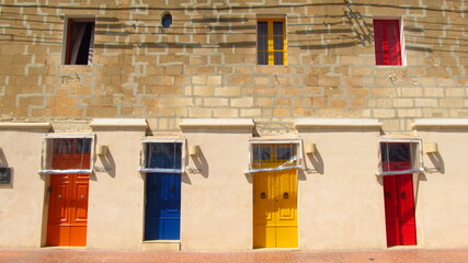 Różnokolorowe pomalowane stare drzwi i okiennice na tle starego zadbanego domu na Malcie - obrazy, fototapety, plakaty