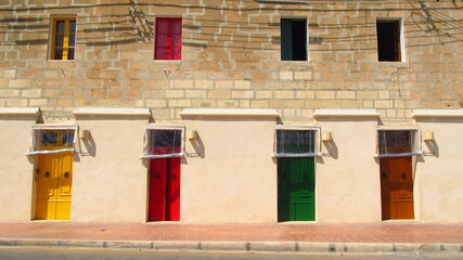 Różnokolorowe pomalowane stare drzwi i okiennice na tle starego zadbanego domu na Malcie