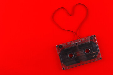 Old black audio cassette on a red background with a heart made of film. Cassette heart
