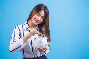Fototapeta na wymiar Beautiful young Asian woman putting coins in piggy bank on blue background.