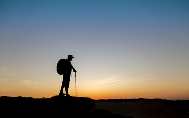 Silhouette of old man achieve hiking on peak with view sunset. Elderly man hiking in mountains on holiday