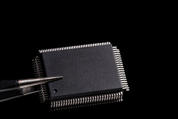 Close-up photos, IC microchip in tweezers on black background.