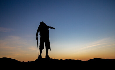 Silhouette of old man achieve hiking on peak with view sunset. Elderly man hiking in mountains on holiday