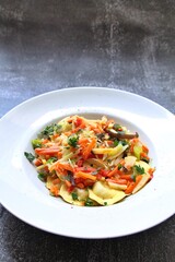 white plate with round ravioli and lots of different vegetables, thinly sliced vegetables and Italian dumplings, egg pasta ravioli, Italian dumplings, mixed vegetables