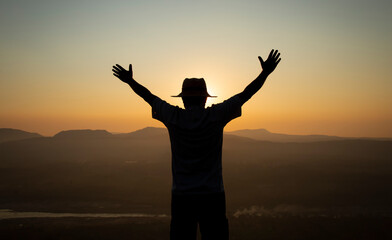 Fototapeta na wymiar Successful silhouette hiker man standing raised hands on top of mountain, enjoying nature view during sunrise.