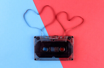 Old black audio cassette on a red and blue background with two film hearts. Cassette hearts
