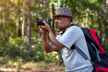 An elderly Asian man with backpack using camera while hiking in nature