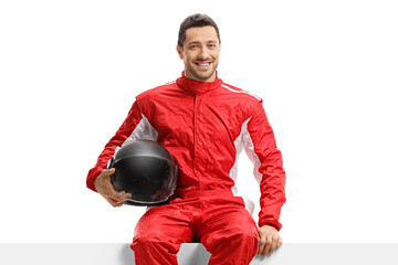 Car racer in a red uniform sitting on a panel holding a helmet