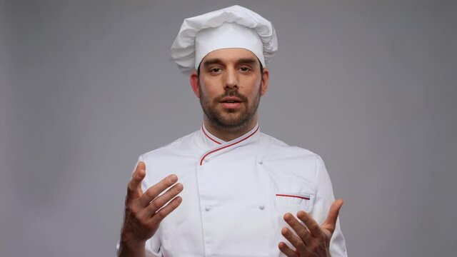 cooking, culinary and blogging concept - happy smiling male chef in toque and jacket videoblogging and talking on camera over grey background