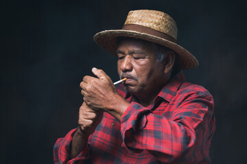 An elderly Asian man wearing a hat and smoking cigarette on black background. Taking a photo in studio
