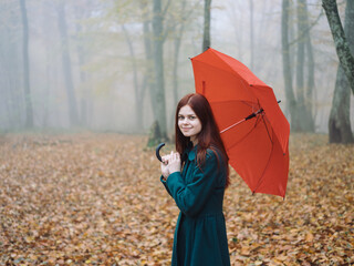 Pretty woman red umbrella walk in autumn in the forest with fog yellow leaves