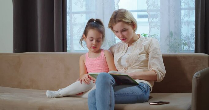 A caring mother helps her daughter with homework, a parent mother teaches a preschool child to read a book. Learning to read learning at home, family education together