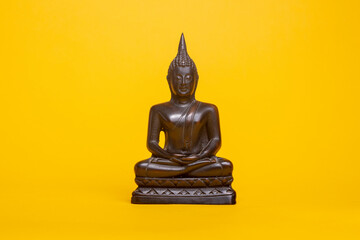 Small bronze Thai buddha statue against a yellow seamless background in meditative posture