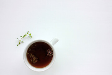 Cup of herbal oregano tea with dry marjoram flowers and Anise hyssop green leaves on white table background with copy space. Top view. Flat lay composition