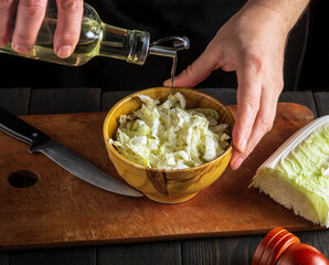Man chef adding oil to napa cabbage salad. The idea of making a diet breakfast or dinner