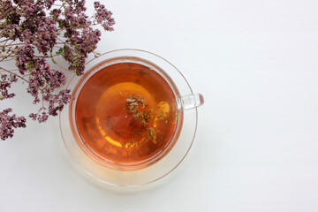Glass cup of herbal tea with dry oregano flowers on white table background with copy space. Top view.