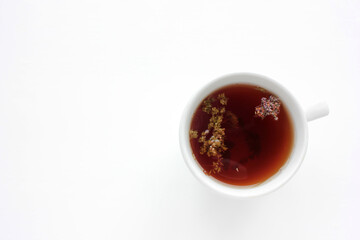 Cup of herbal oregano tea with dry marjoram flowers on white table background with copy space. Top view. Flat lay composition