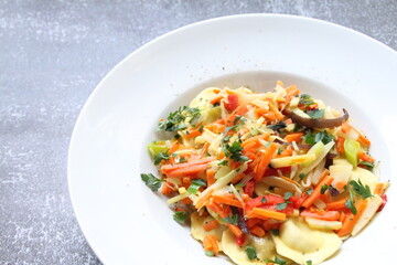 white plate with round ravioli and lots of different vegetables, thinly sliced vegetables and Italian dumplings, egg pasta ravioli, Italian dumplings, mixed vegetables