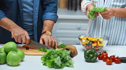 cropped view of senior man cutting lettuce while preparing breakfast near wife
