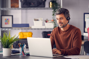 Mature Businessman Wearing Telephone Headset Talking To Caller In Customer Services Department