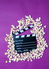 Movie clapperboard and popcorn on purple background Conceptual for cinema