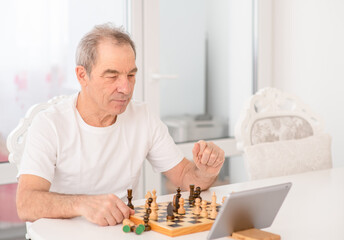 Senior man uses tablet computer to play chess with her friends during quarantine Coronavirus (Covid-19) epidemic