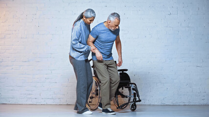 elderly asian woman supporting disabled husband near wheelchair