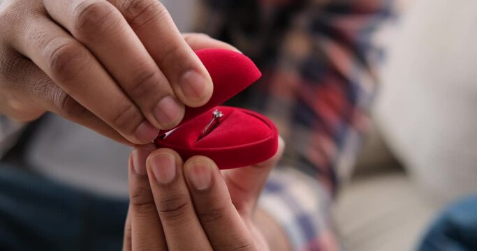 Man holding red gift box with engagement ring at home