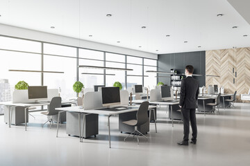 Businessman in black suit in modern sunny spacious coworking office with modern furniture, wooden...