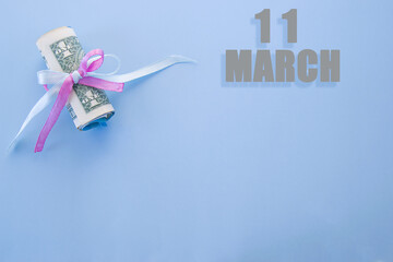 calendar date on blue background with rolled up dollar bills pinned by blue and pink ribbon with copy space. March 11 is the eleventh day of the month