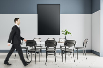 Businessman walking by big white dining table with black chairs around and black poster with copyspace on the wall. Mockup