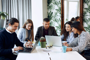 A young group of business people are discussing a new business plan, working on laptops while sitting in a modern office.