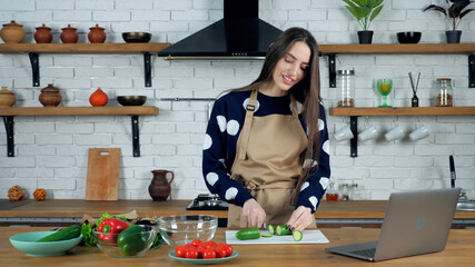 Smiling housewife listen chef teacher sliced fresh cucumber study online video call conference webcam chat laptop. Beautiful woman in home kitchen watching culinary cook webinar course lesson computer