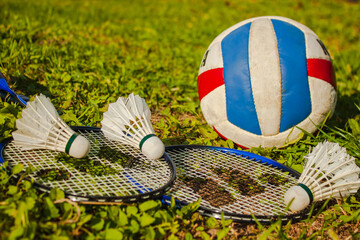 Three shuttlecocks, two badminton rackets and a volleyball ball on the grass