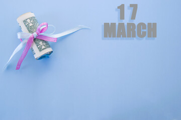 calendar date on blue background with rolled up dollar bills pinned by blue and pink ribbon with copy space. March 17 is the seventeenth day of the month