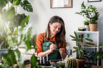 A happy young woman enjoys time at her homegarden labeling seed trays. Seed-starting plants in the...