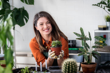 Woman taking care of plants at her home. Smiling young woman holding a succulent plant.
