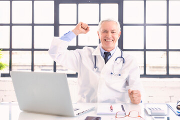 Successful male doctor portrait while sitting behind his laptop at the doctor's office