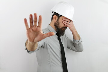 Builder man wearing hardhat and reflecting jacket in shock covering face and eyes with hand with embarrassed expression and doing stop gesture with fear expression.