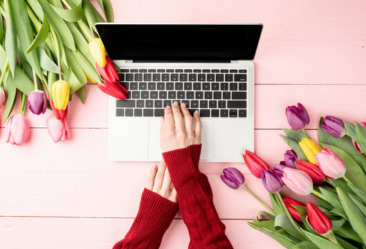 Woman hands typing on laptop keyboard. Feminime worlspace decorated with tulips