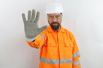 Bearded man wearing hardhat, safety goggles and reflecting jacket, rejection expression crossing fingers doing negative sign