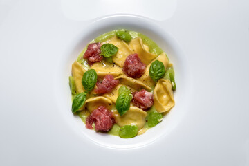 Ravioli del plin with broad beans sauce, Bra sausage and basil leaves, typical stuffed pasta from Langhe, Italy. Top view