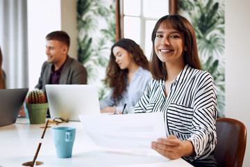 Beautiful caucasian business woman with a cup of coffee or tea working at a laptop sitting at an office table with her colleagues.