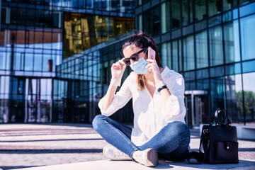 Fototapeta premium Confident woman wearing face mask while sitting on the street and making a call