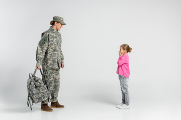 Cheerful woman in camouflage looking at daughter on grey background