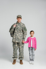 Soldier with backpack holding hand of daughter on grey background