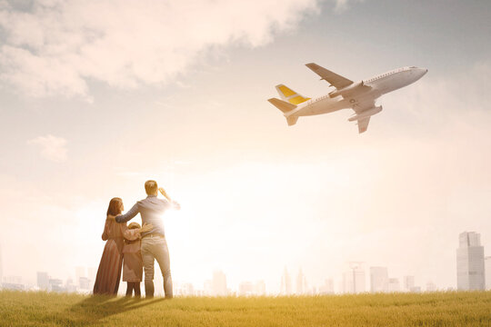 Happy Family Looking At Flying Airplane In Dusk Sky