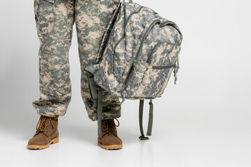 Cropped view of soldier in uniform holding backpack on grey background
