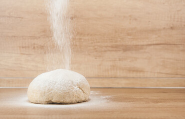 Ball of pizza dough on a wooden background with dusting of flour