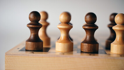 Close up of black and white wooden chess pieces on white background. Selective focus on black pawn.